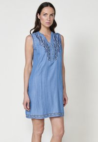 Robe en denim avec un col en V, sans manches, en tissu bleu, fermeture à boutons sur le devant et broderie bleue détaillée le long du col et de l'ourlet.