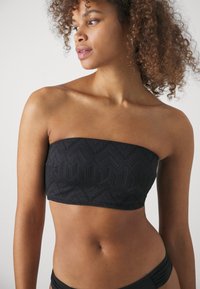 Juodas be petnešėlių bikini viršus su raukšlėtu zigzago raštu, sukurtas su glotnia apdaila ir be siūlių kraštais, užtikrinant tvirtą prigludimą.