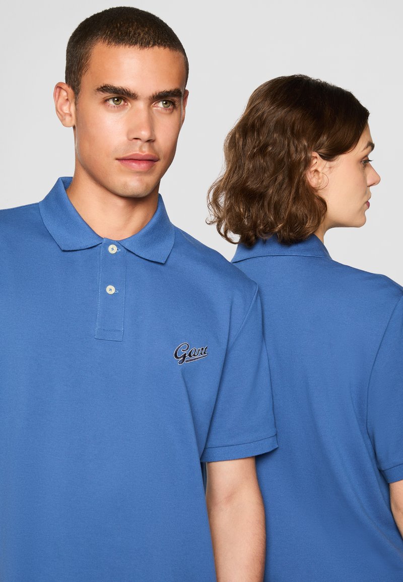 Polo bleu avec col, arborant un petit logo brodé sur la poitrine gauche. Fabriqué en tissu texturé, il a des manches courtes et une coupe décontractée.