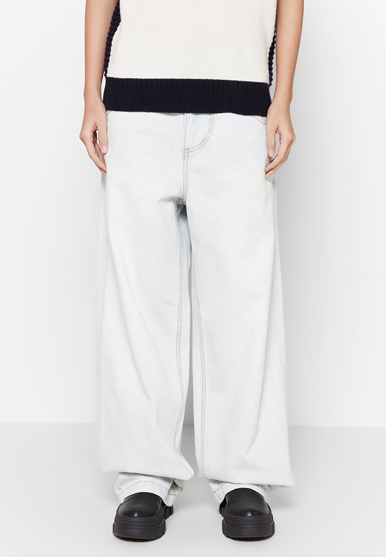 Jean en denim léger avec des jambes évasées et taille haute, présentant des coutures visibles et une texture de tissu usé. Associé à des chaussures à plateforme noires.