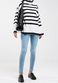 Randig svart och vit tröja med hög krage, tillsammans med ljusblå skinny jeans och svarta slip-on skor. Har en avslappnad passform.