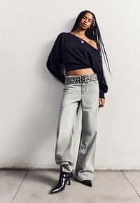Črn off-shoulder pulover, svetlo sivi ohlapni kavbojke in črne špičaste gležnjarje z sijajnim zaključkom. Okrasen črno-beli pas.