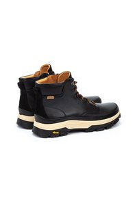 Botas de tobillo de cuero negro con forro marrón, cordones marrones y suelas de goma beige. Presentan un logo de Vibram y un diseño texturizado.