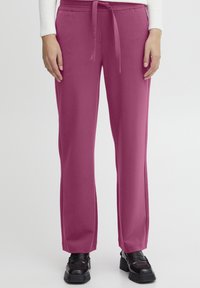 Pantalons roses à jambe large avec une taille à cordon, présentant un tissu lisse et texturé et une coupe décontractée. Associés à des chaussures à plateforme noires.