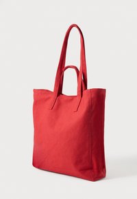 Czerwona torba na ramię wykonana z bawełnianego płótna, posiadająca dwa długie uchwyty, usztywniony kształt oraz gładką teksturę bez widocznych wzorów i akcentów.