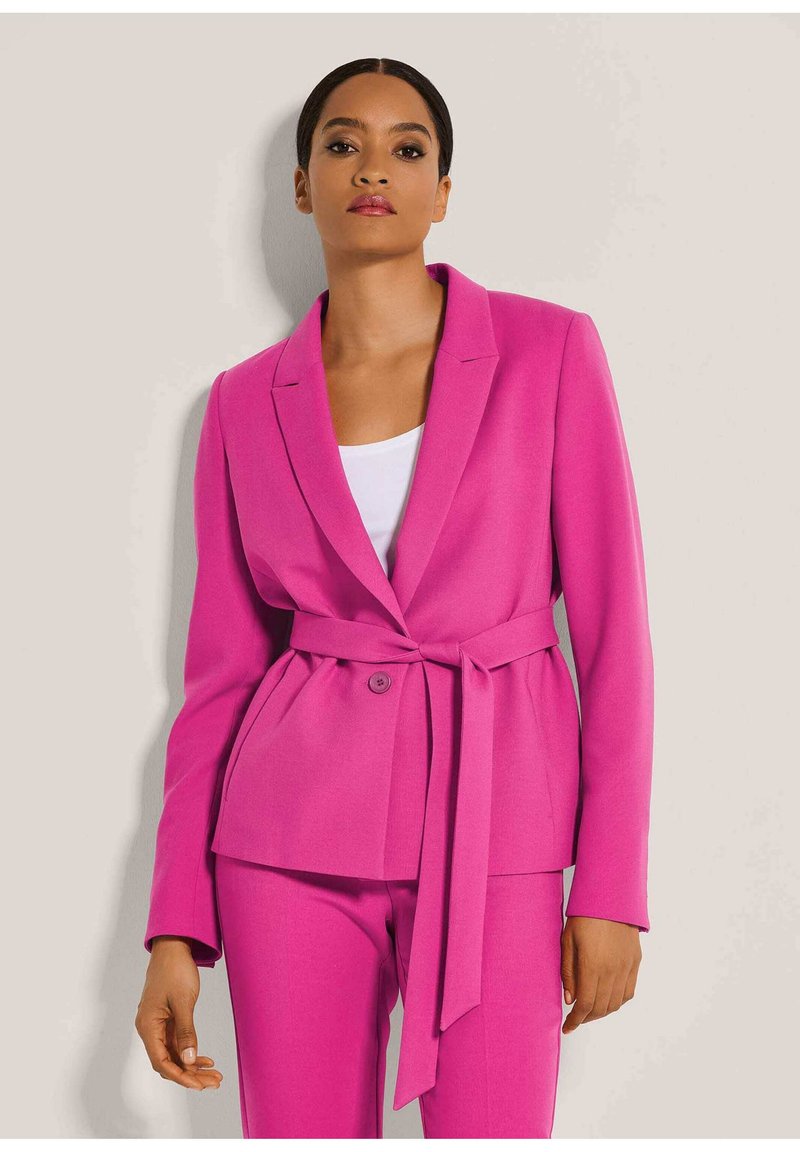 Fuchsia Blazer mit taillierter Passform, Reverskragen, einreihigem Knopfverschluss und gebundenem Gürtel in der Taille, kombiniert mit passenden Hosen.