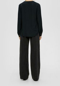 Camicia nera a maniche lunghe con orlo arrotondato, abbinata a pantaloni larghi scuri. La camicia presenta polsini con bottoni e una texture morbida.