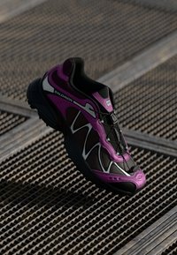 Black and purple athletic shoe with a textured mesh upper, reflective accents, and a cushioned sole. Features a lace-up design.