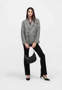 Veste grise croisée à boutons noirs, associée à un pantalon noir et un sac hobo noir. Design élégant et cintré, avec des talons pointus.