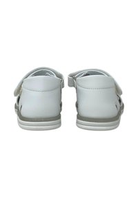 Sandali bianchi in pelle con una fascia in Velcro, design aperto sul retro e soletta testurizzata. Suola piatta con una leggera accentuazione grigia.