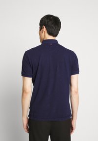 Mørkeblå polo-shirt lavet af bomuld, med krave og korte ærmer. Indeholder en diskret logo detalje nær halsen.