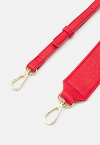 Červený kožený popruh s texturovaným povrchem, obsahující zlaté kovové prvky a odnímatelné sponky typu humrová na obou koncích.