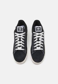 Sorte ruskind sneakers med hvide snørebånd og en struktureret gummisål. Indehaver Adidas-logo på tungen og kontrastsyet langs siderne.