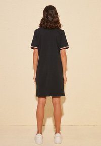 Černé šaty s krátkými rukávy, zdobené pruhovanými akcenty v červené, bílé a modré barvě na okrajích rukávů. Hladká textura, silueta délky ke kolenům.