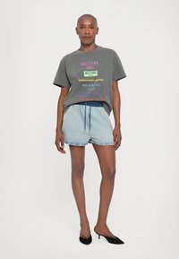 Grå T-skjorte med flerfarget "Moschino Jeans" tekst, parret med lyseblå denimshorts med elastisk midjebånd og snøring.