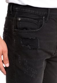 Musta farkut, joissa on kuluneet yksityiskohdat, repaleiset kohdistukset ja klassinen viisi taskua -muotoilu. Sileä rakenne ja slim fit -malli.