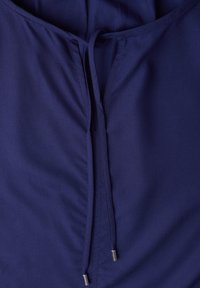 Top in tessuto blu navy con chiusura a coulisse e punte metalliche, caratterizzato da una texture morbida e liscia e dettagli raccolti sottili.
