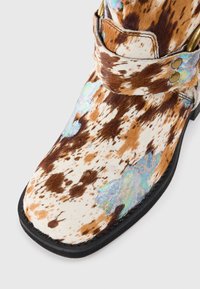 Botas con un patrón de manchas multicolores, que presentan una parte superior de terciopelo marrón y crema, acentuada con detalles iridiscentes y cierre de hardware dorado.
