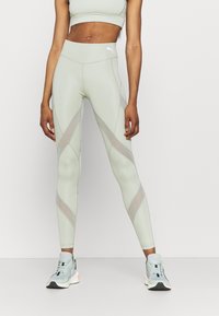Leggings vert clair avec une taille haute, comportant des panneaux en maille découpés selon un motif géométrique. Confectionnés dans un tissu extensible à la texture lisse.