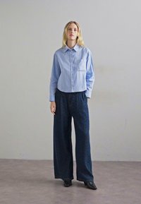 Ανοιχτό μπλε πουκάμισο με γιακά, συνδυασμένο με σκούρες ραφές και φαρδιές παντελόνες. Μαύρες μπότες μέχρι τον αστράγαλο ολοκληρώνουν το σύνολο.