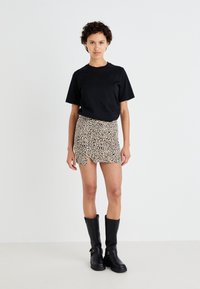 Svart oversized t-skjorte, kort leopardmønstret skjørt med sprekk, og knelangne svarte støvler. Glatt stoff med kontrasterende mønstre.