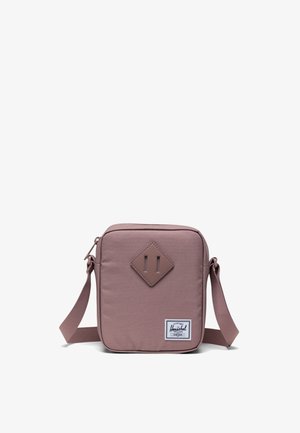 Quadratische mauve Umhängetasche mit verstellbarem Riemen, vorderer Diamantapplikation und weißem rechteckigen Herschel-Logo in der unteren Ecke.