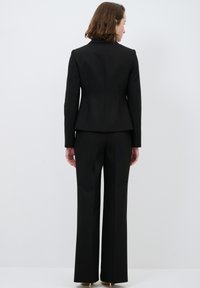 Czarna marynarka dopasowana w talii, zaprojektowana z wyraźnymi ramionami i długimi rękawami, w połączeniu z szerokimi czarnymi spodniami.