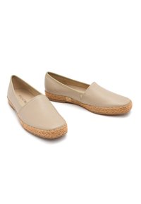 Beżowe skórzane buty typu slip-on z zaokrąglonym noskiem, korkową podeszwą i plecionym wykończeniem wzdłuż krawędzi. Gładka tekstura z minimalnymi akcentami.