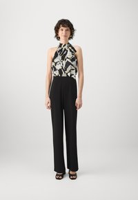 Sorte jumpsuit med et mønstrete, ermeløst topp med halterneck-design. Stoffet er glatt og faller ned til vide bukser.