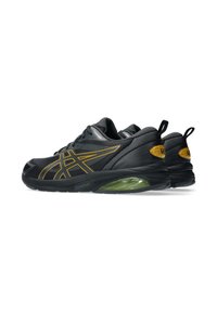 Zapatillas deportivas negras con detalles amarillos, parte superior de malla texturizada, diseño elegante y entresuela acolchada verde. Presenta una punta redondeada y cierre de cordones.