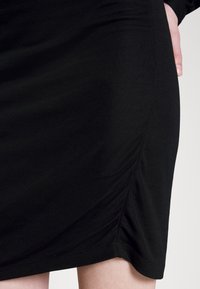 Czarna dopasowana sukienka wykonana z gładkiego, elastycznego materiału. Posiada marszczone boki oraz zakrzywiony dół, co nadaje sylwetce konturowany kształt.