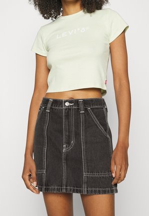 Femme portant un t-shirt court Levi's vert pâle et une jupe en denim noire taille haute avec des coutures blanches et des poches avant.