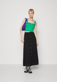Zöld, bordázott cropped top fodros szegéllyel, fekete maxi szoknya elülső gombokkal, és lila textúrájú kézi táska. Ezüst platform cipők.