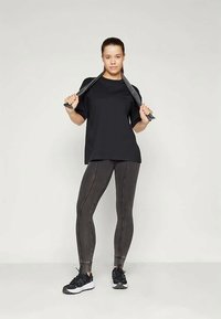 Μαύρο κοντομάνικο μπλουζάκι με χαλαρή γραμμή, συνδυασμένο με σκούρες, υφασμάτινες κολάν που παρουσιάζουν αντίθετα ραφές και κολλητή εφαρμογή.