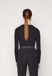 Maglia nera a maniche lunghe con design aderente, caratterizzata da una vita arricciata accentuata da una elegante fascia bianca a righe. Texture liscia.