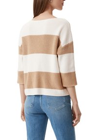 Sweter w paski w kolorze kremowym i brązowym, o luźnym kroju, z rękawami o długości 3/4, z fakturowanej tkaniny dzianinowej oraz z prążkowanymi mankietami. Zestawiony z niebieskimi dżinsami.