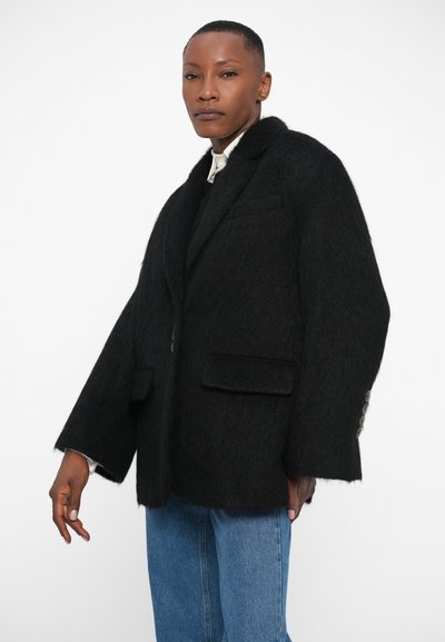 Črn blazer iz volnene mešanice z teksturiranim zaključkom, v oversized kroju in s klasičnim ovratnikom. Ima dva sprednja žepa in gumbne detajle na rokavih.