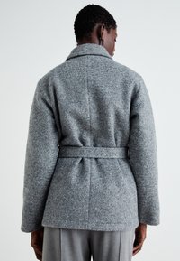 Grauer Wollmantel mit tailliertem Gürtel, Schalkragen und strukturierter Oberfläche. Verfügt über weite Ärmel und Nahtdetails.