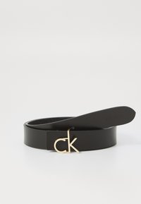 Čierny kožený opasok s prackou v zlatej farbe s logom "ck" a hladkým povrchom, navrhnutý pre odolnosť a štýl.
