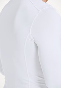 Witte sportieve longsleeve top van glad, rekbaar materiaal met een textuurpaneel aan de zijkant en platte naden voor extra comfort.