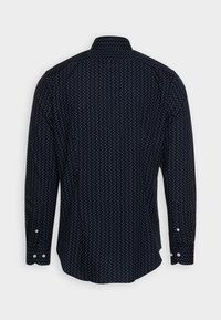 Marineblauwe lange mouwen knoopshirt met witte stippen, gezien vanaf de achterkant tegen een effen achtergrond.