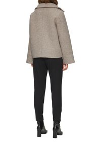 Manteau en mélange de laine taupe avec un large col, de longues manches et une coupe décontractée, associé à un pantalon noir et des bottines.