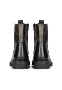 Botas de tobillo de cuero negro con cierres de cremallera, acentos verticales dorados y una suela de goma texturizada, que presentan un acabado suave y una punta redondeada.
