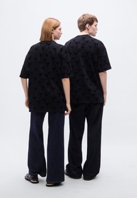 Μαύρα υπερμεγέθη t-shirt με υφή, συνδυασμένα με σκουρόχρωμα τζιν με ίσια πόδια. Η πίσω όψη δείχνει άνετη εφαρμογή και ελάχιστες λεπτομέρειες.