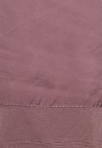 Hladká mauve tkanina s viditelným švem a drobnými vráskami, ukazující přechod mezi dvěma texturami tkanin.
