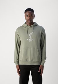 Sweat-shirt à capuche vert olive avec une poche avant, présentant un logo graphique blanc "MAKIA CO." et des cordons de serrage réglables au niveau de la capuche.