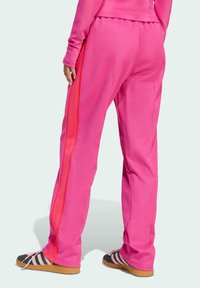 Roze trainingsbroek van zacht materiaal met rode zijstrepen, een losse pasvorm en zakken. Gecombineerd met zwarte schoenen en roze accenten.