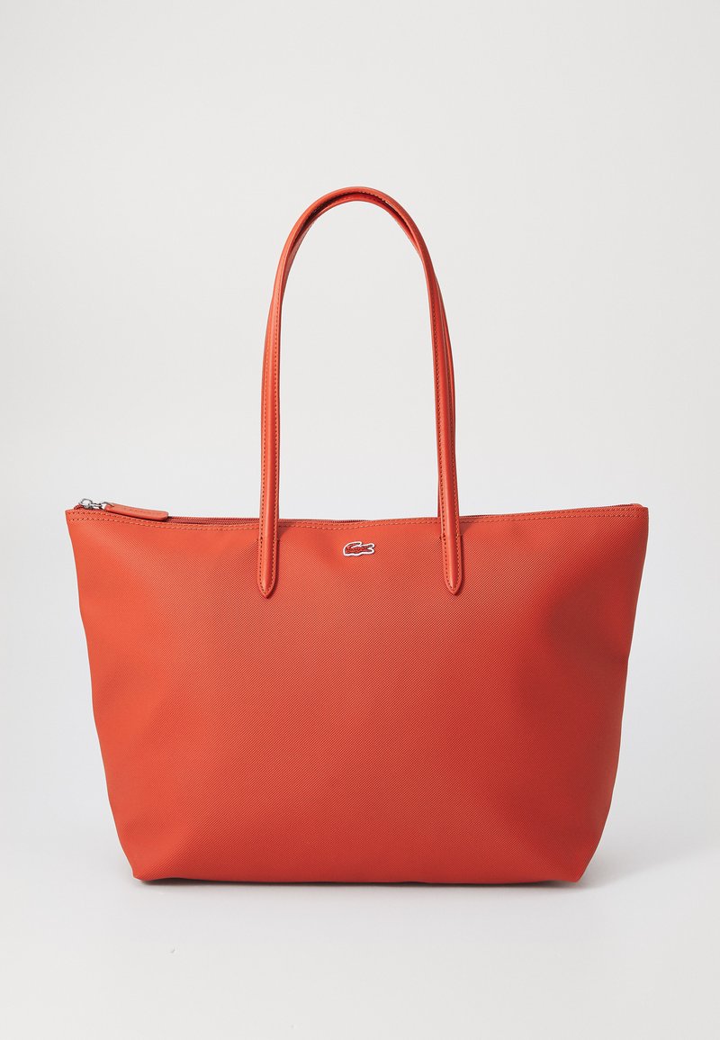 Röd tote-väska med två långa handtag, texturerat syntetmaterial, dragkedjestängning och en liten Lacoste-logotyp på framsidan.