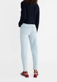 Ljusblå denimjeans med smal passform och femficksdesign, kombinerade med en marinblå kabelstickad tröja och röda skor med klackblock.