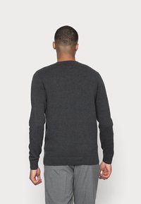 Pull en maille gris foncé avec un motif texturé, col rond, poignets et ourlet côtelés. Porté avec un pantalon gris, vu de dos.